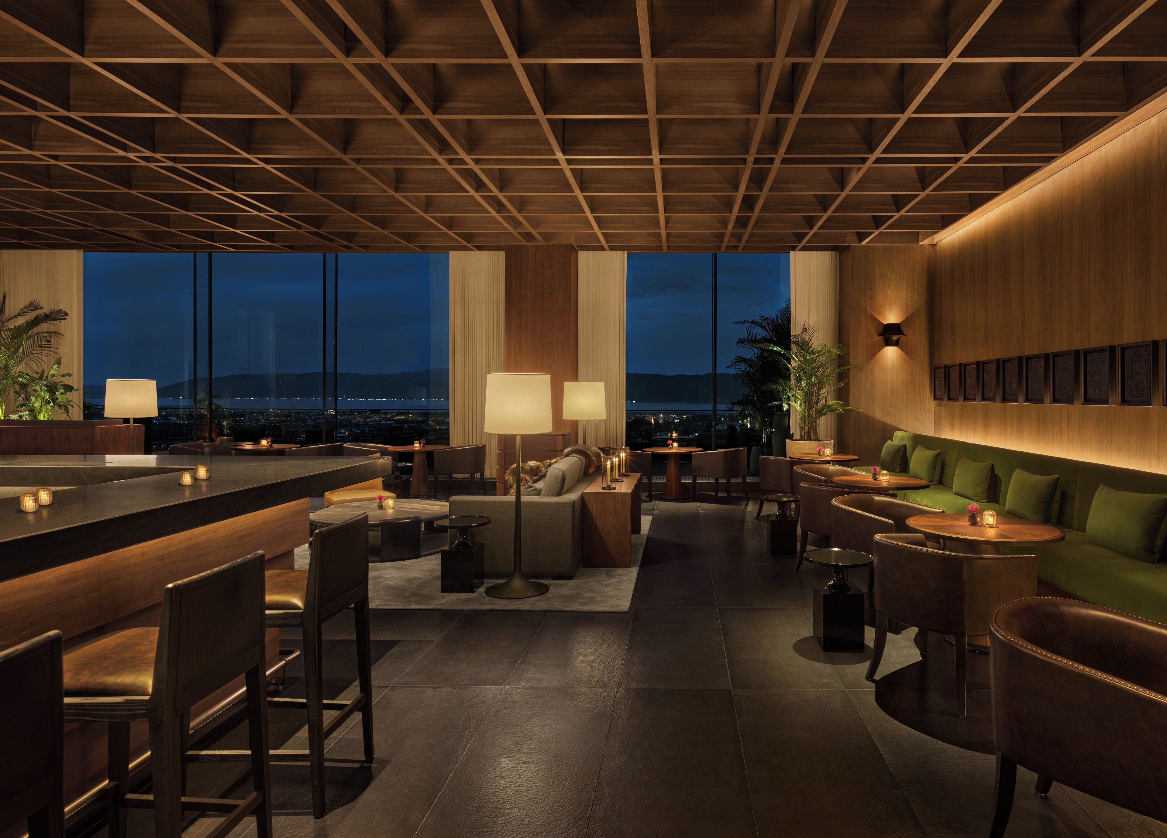 A modern bar area with seating, a high ceiling with wooden beams, and large windows offering a city view.