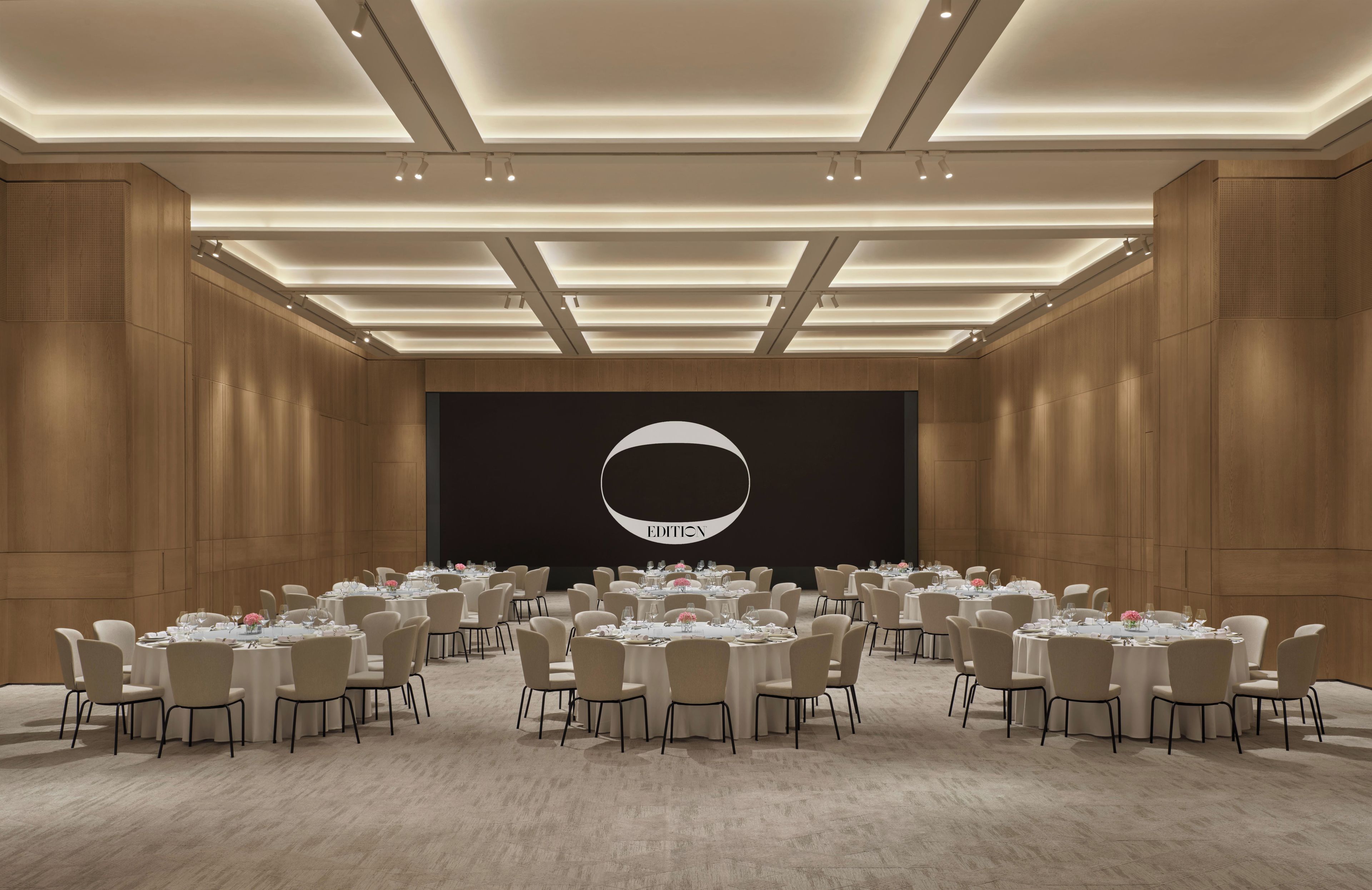A conference room with round tables, chairs, and a large screen displaying the word 'EDITION'.