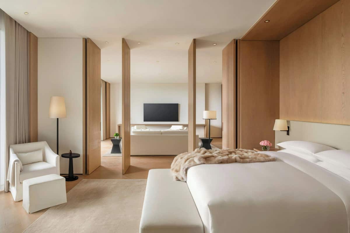 A modern hotel room with a large bed, a sofa, a chair, a TV, and a small table.