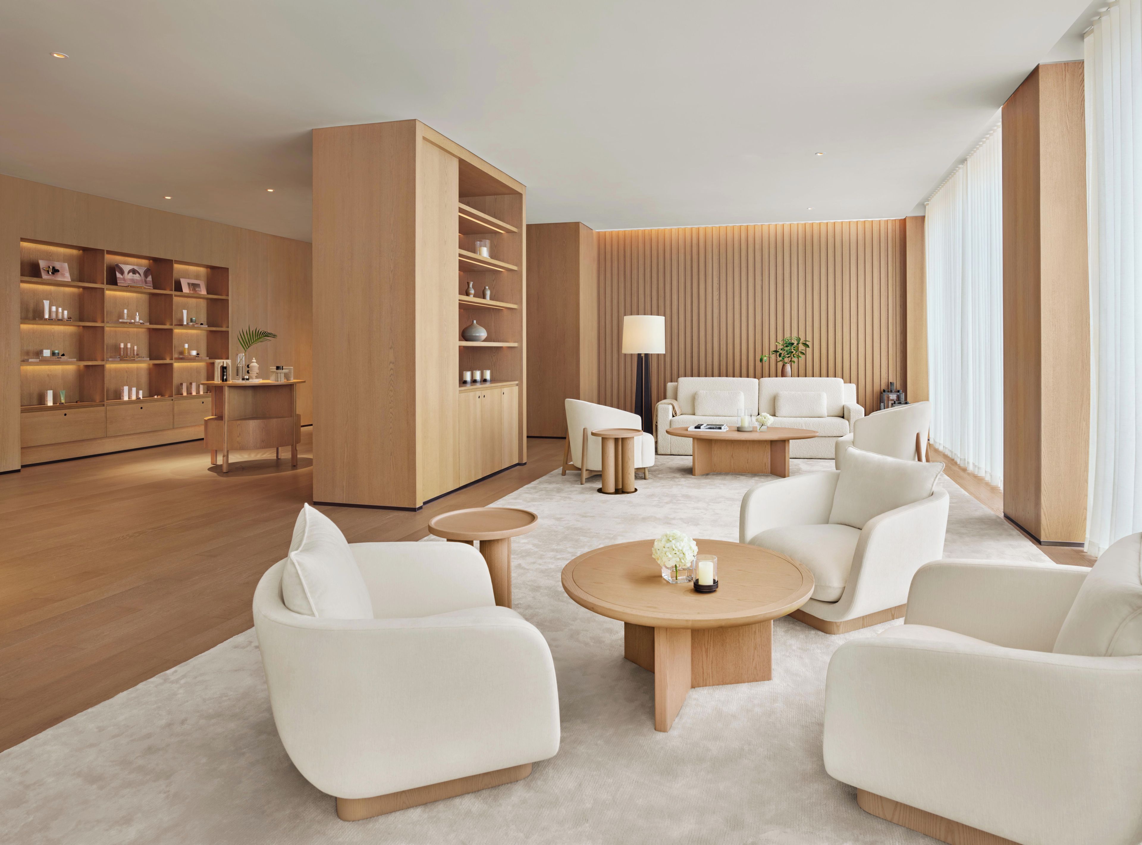 Un hall d’hôtel moderne avec un espace salon central, une grande bibliothèque en bois et une grande fenêtre ornée de rideaux légers.