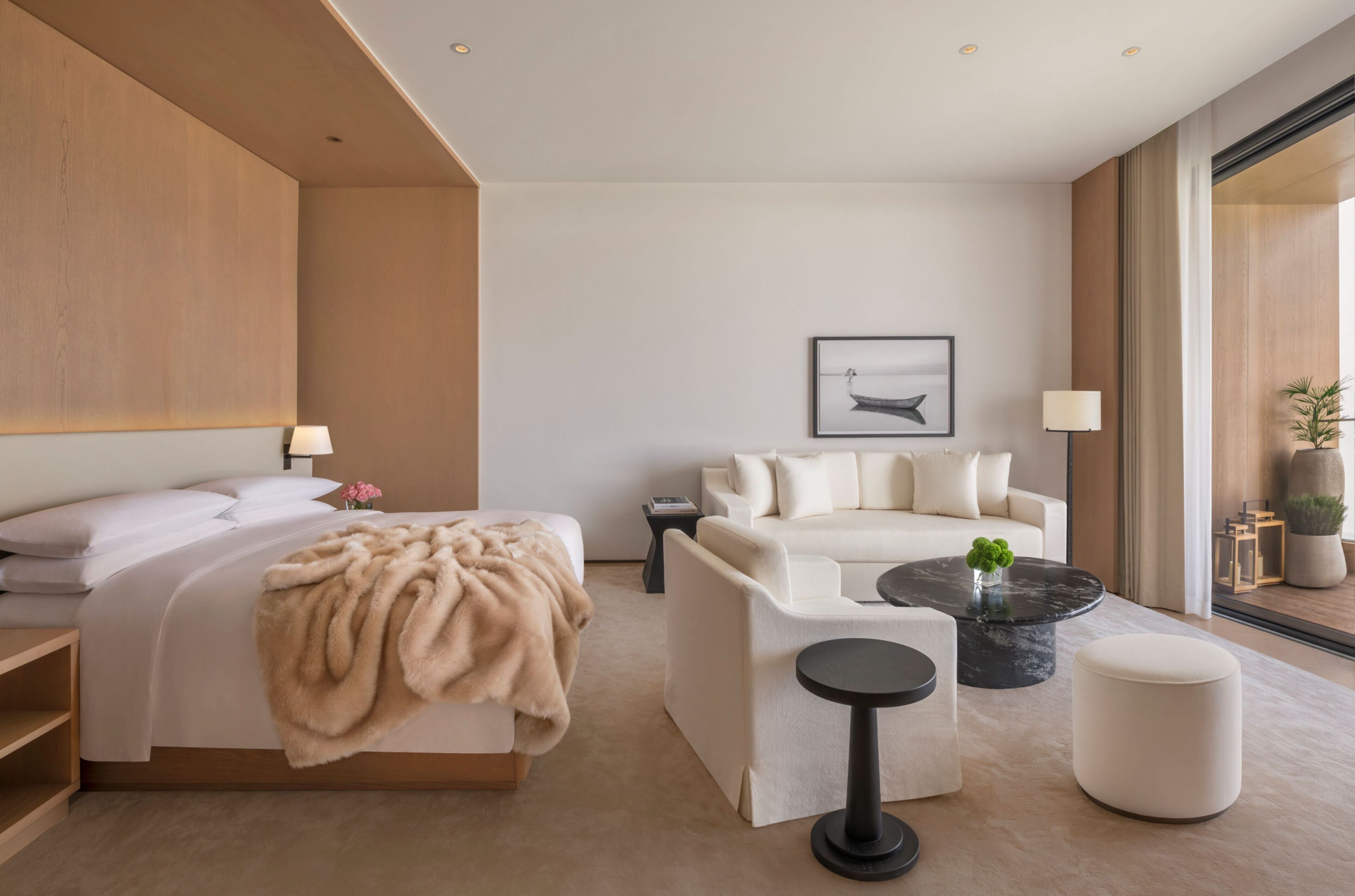 A modern hotel room with a bed, a sofa, a coffee table, and a large window.