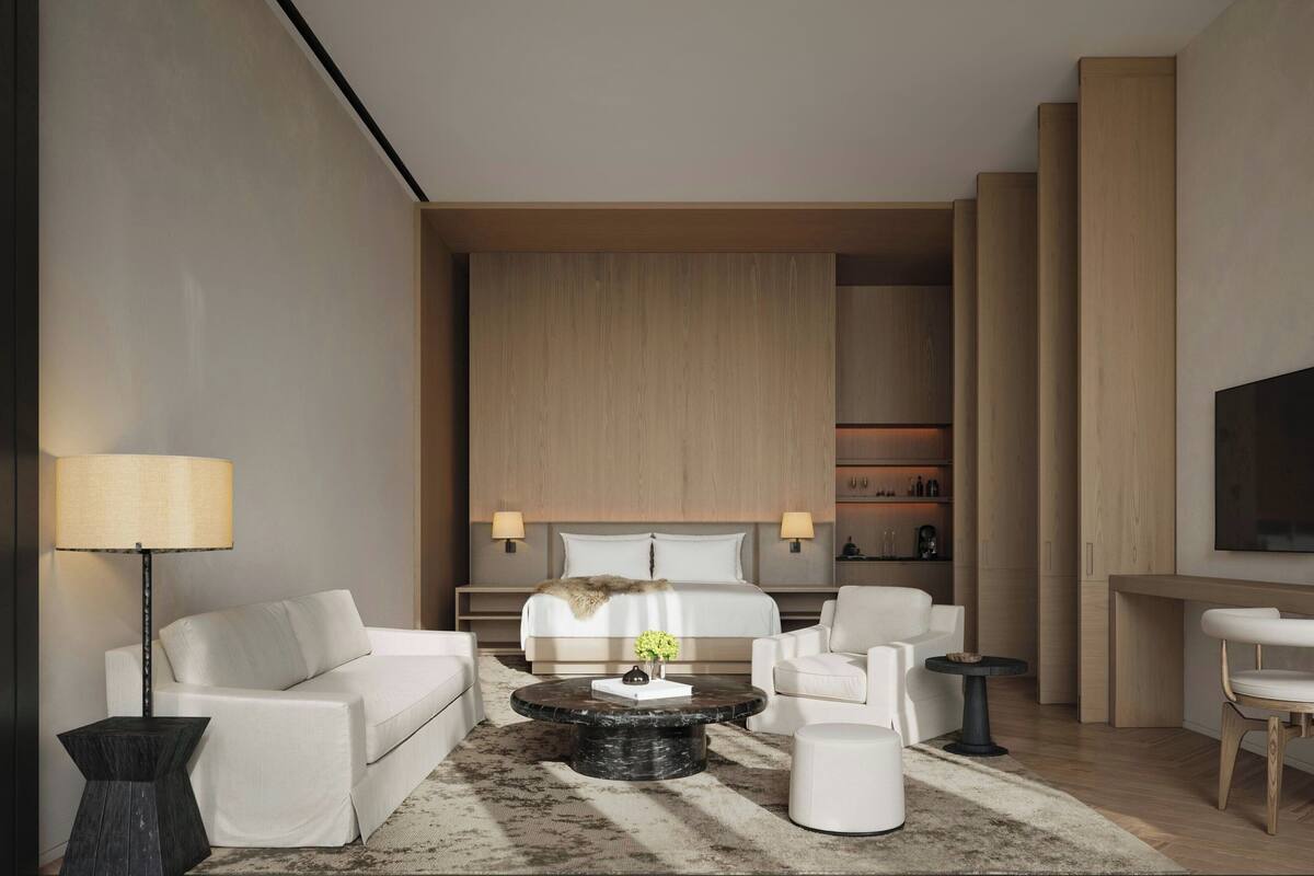 A modern hotel room with a bed, two white sofas, a coffee table, a lamp, and a TV.