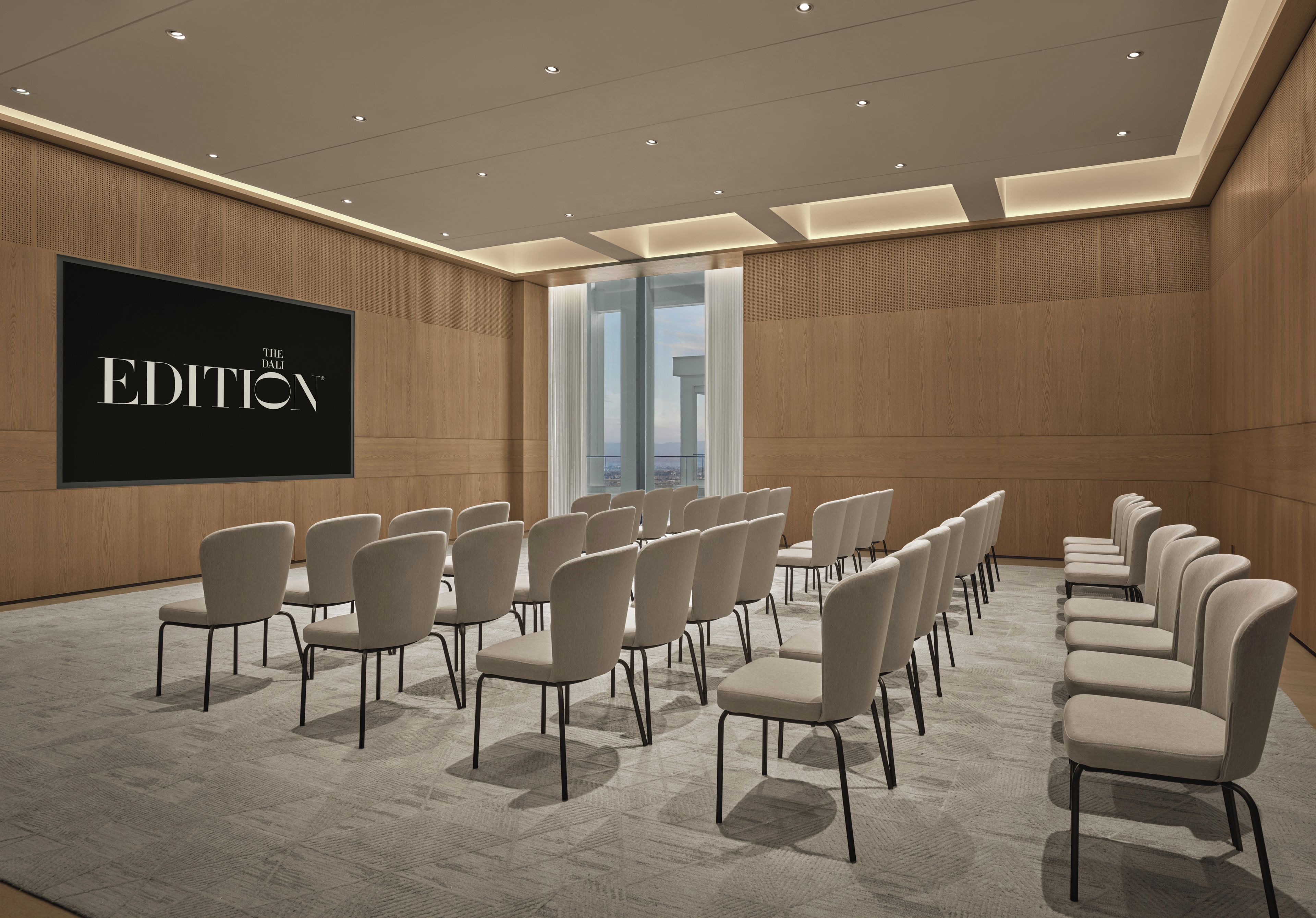 A conference room with a large screen displaying 'THE DALI EDITION' and rows of chairs arranged for a meeting.