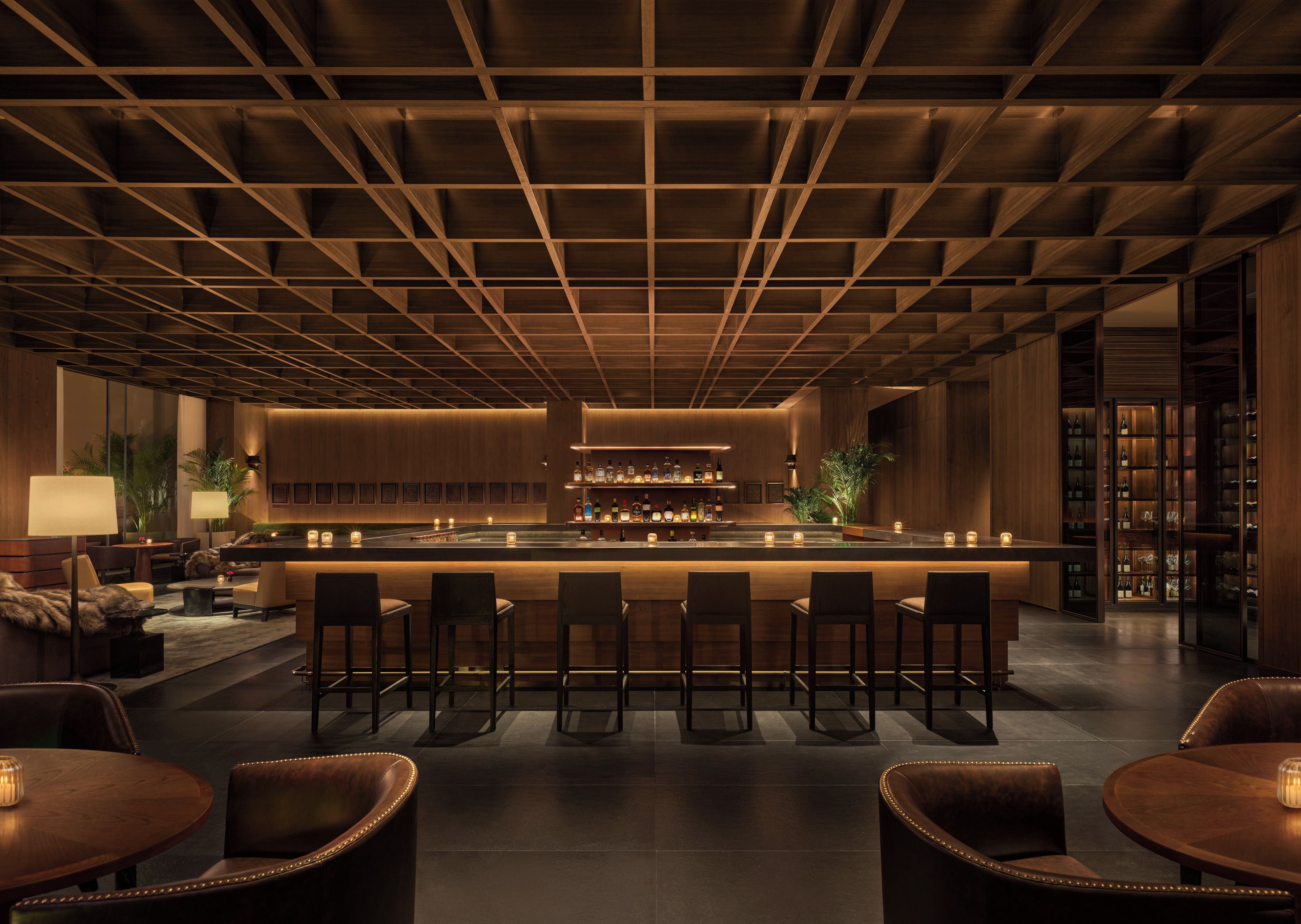 A bar area with a long counter, multiple stools, and a bar stocked with bottles.