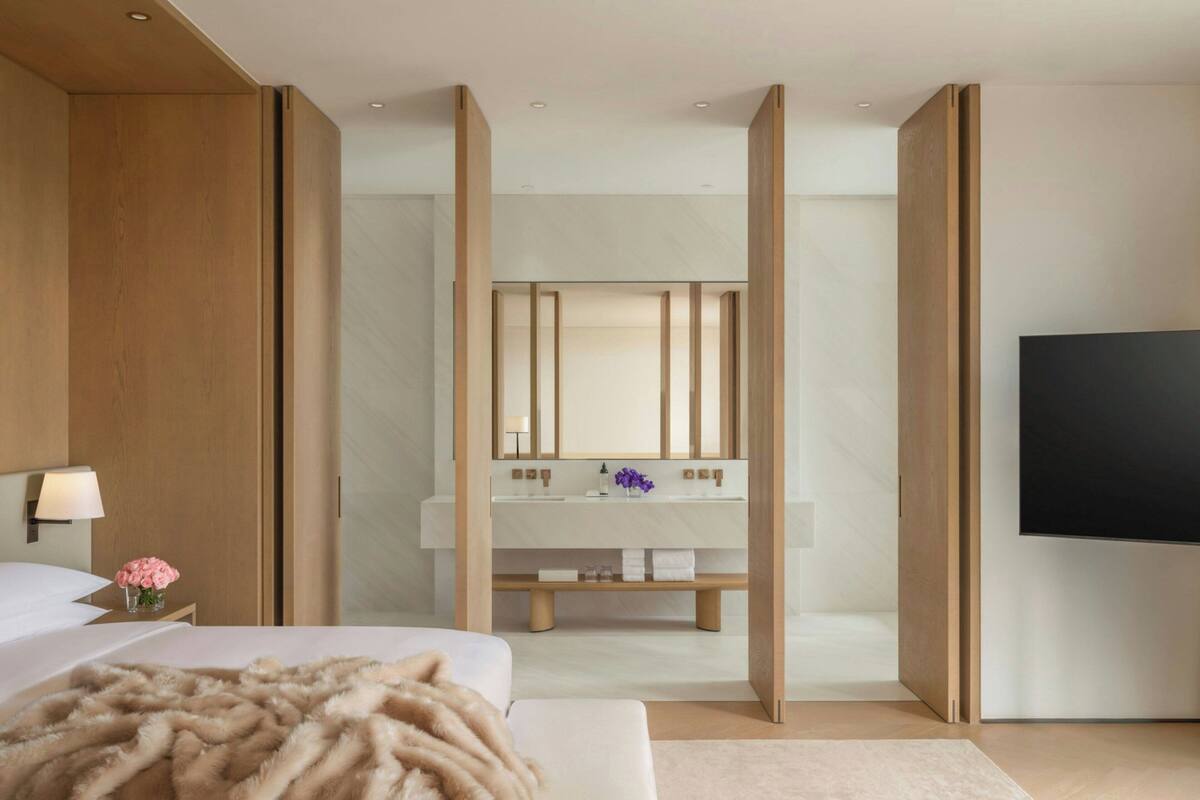 A modern hotel room with a large bed, a TV, a bathroom with a vanity, and a wooden partition.