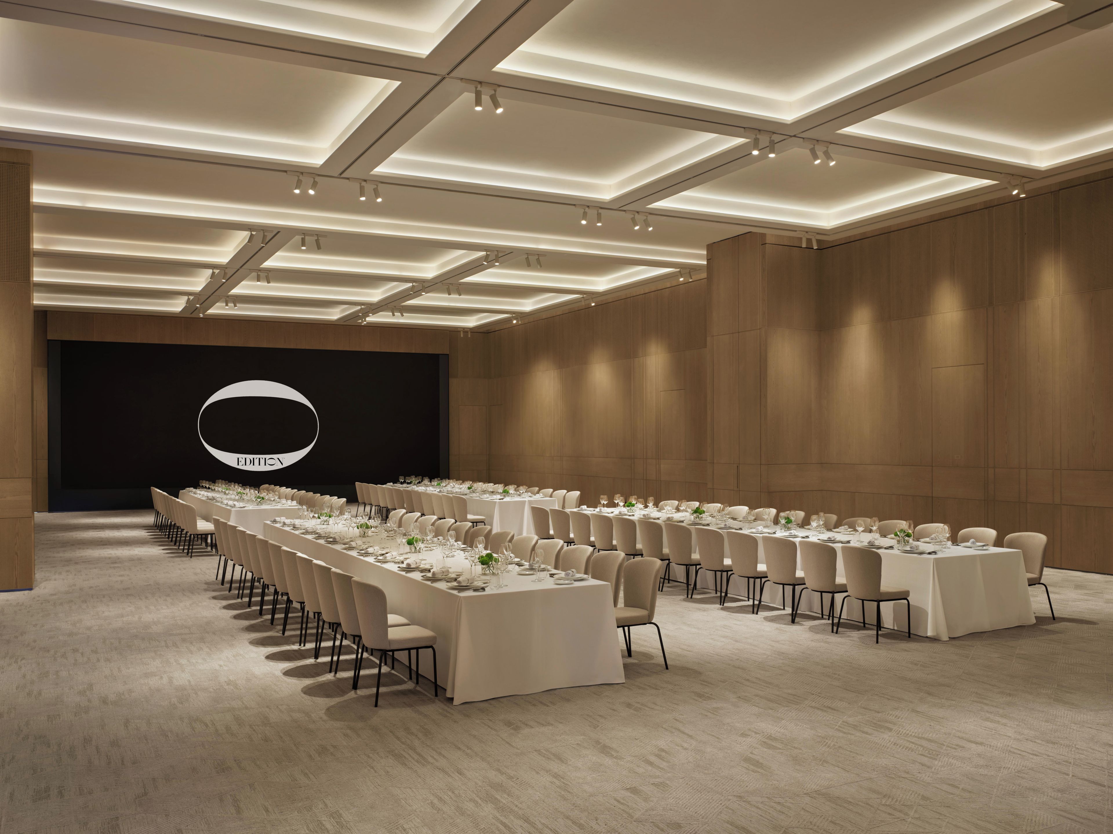 Un salón de conferencias con mesas largas, sillas y un escenario con un logotipo.