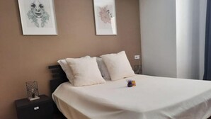 A bedroom with a bed, two pillows, a nightstand, and two framed artworks on the wall.