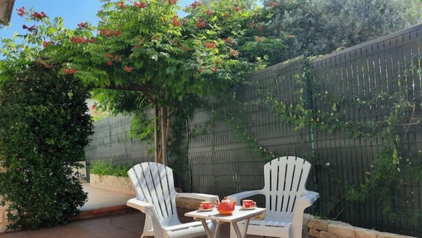 A patio with two white plastic chairs and a small table, surrounded by a brick floor and a wooden fence.