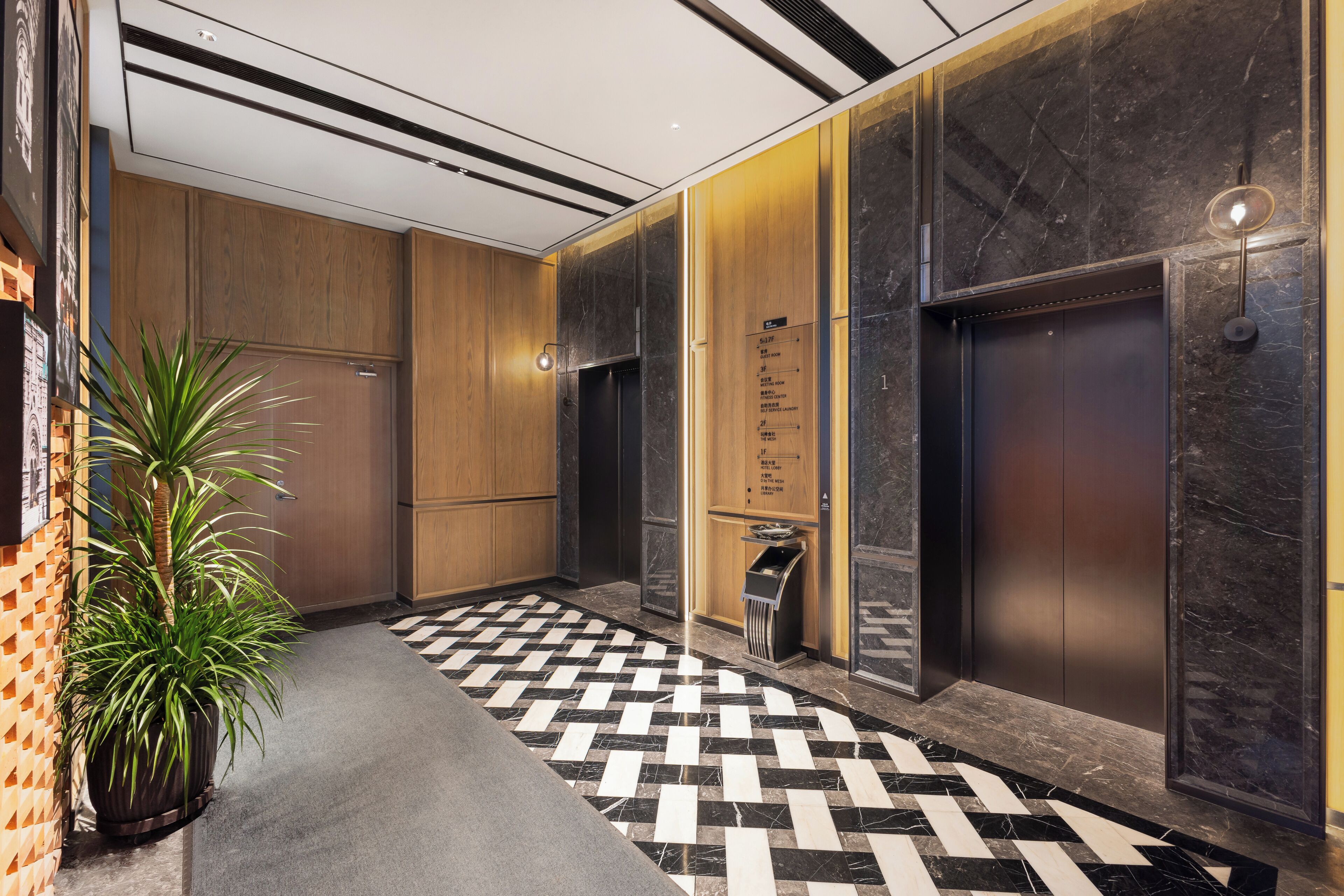 A modern lobby with a checkered floor, wooden panel walls, and two elevators.