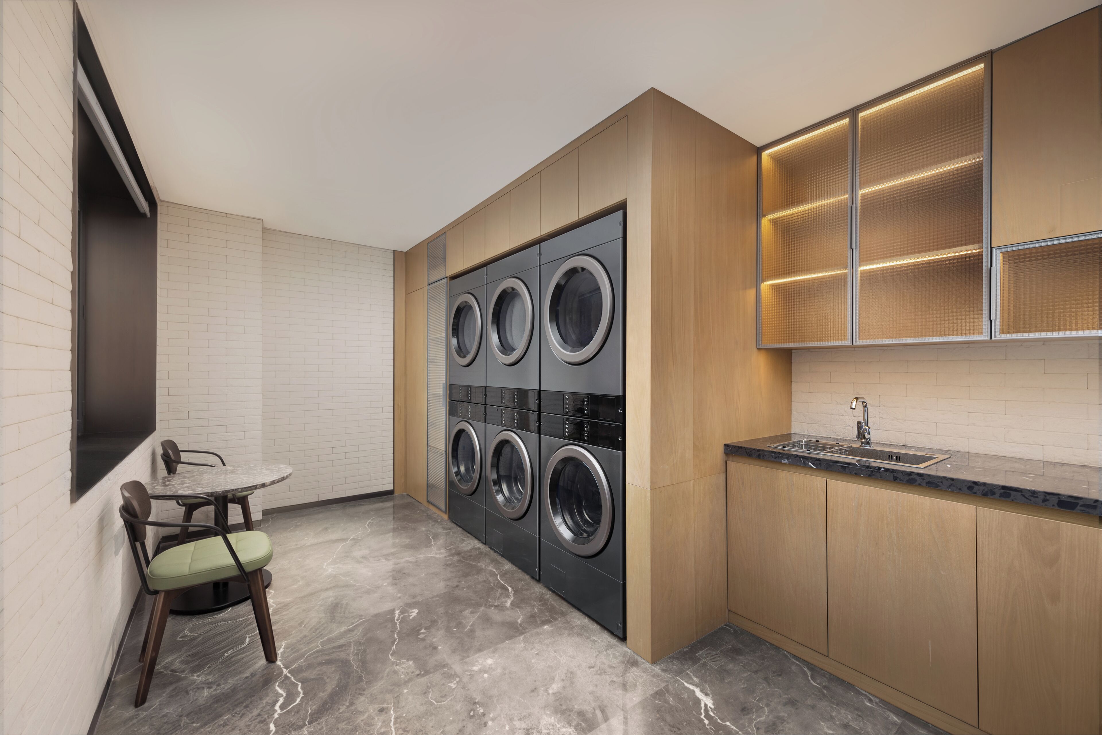 Una cocina funcional con lavadora y secadora integradas, un pequeño comedor con mesa y sillas, y una encimera con lavabo.