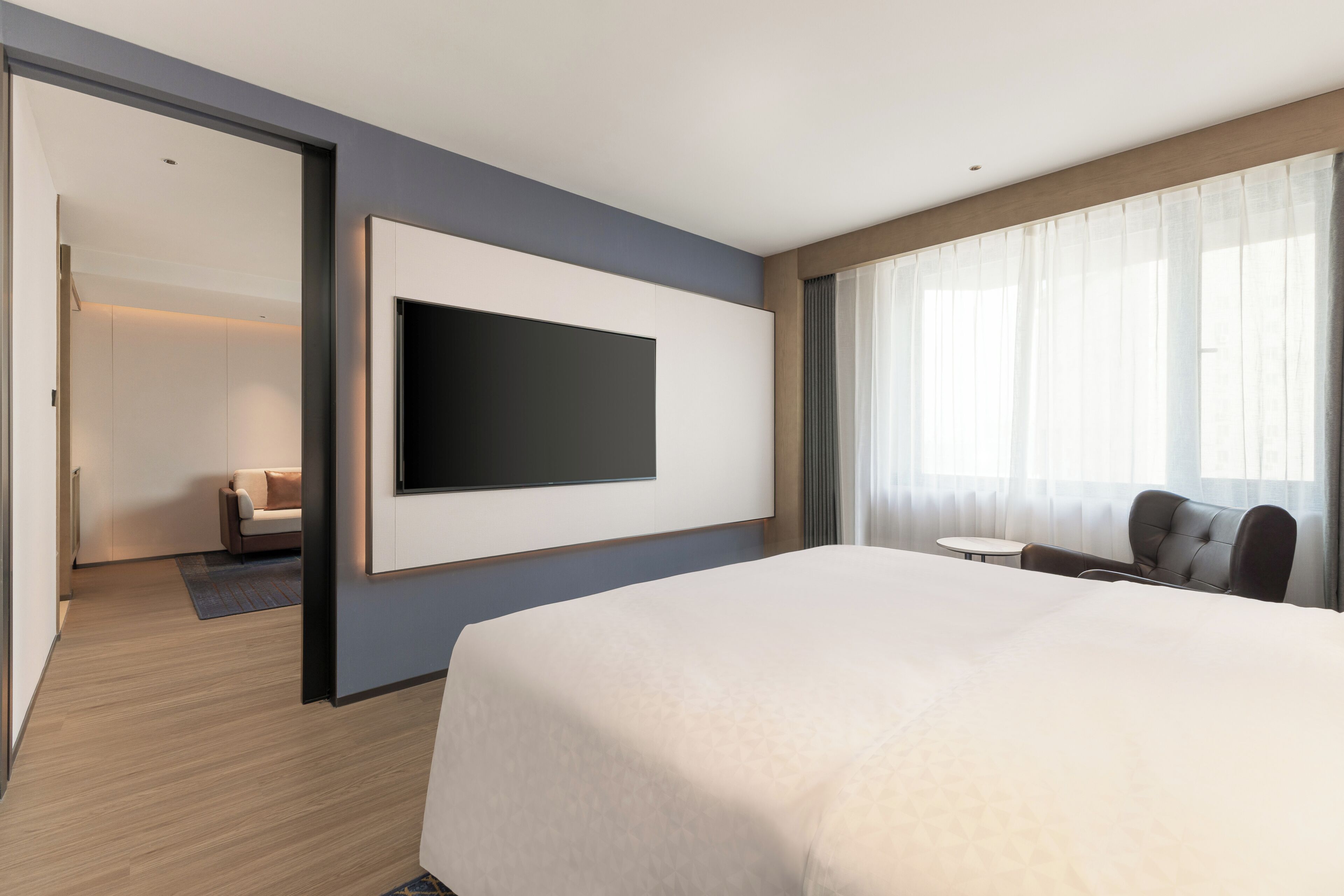 A hotel room with a large bed, a flat-screen TV mounted on the wall, a small round table, and a sofa.