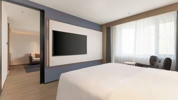 A hotel room with a large bed, a flat-screen TV mounted on the wall, a small round table, and a sofa.
