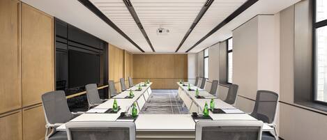 A conference room with a long table, chairs, a projector, and a large screen.
