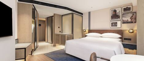 A modern hotel room with a bed, a desk, a chair, a TV, and a wall with framed pictures.