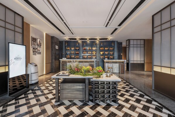 A modern hotel lobby with a check-in counter, a reception desk, and a display board.
