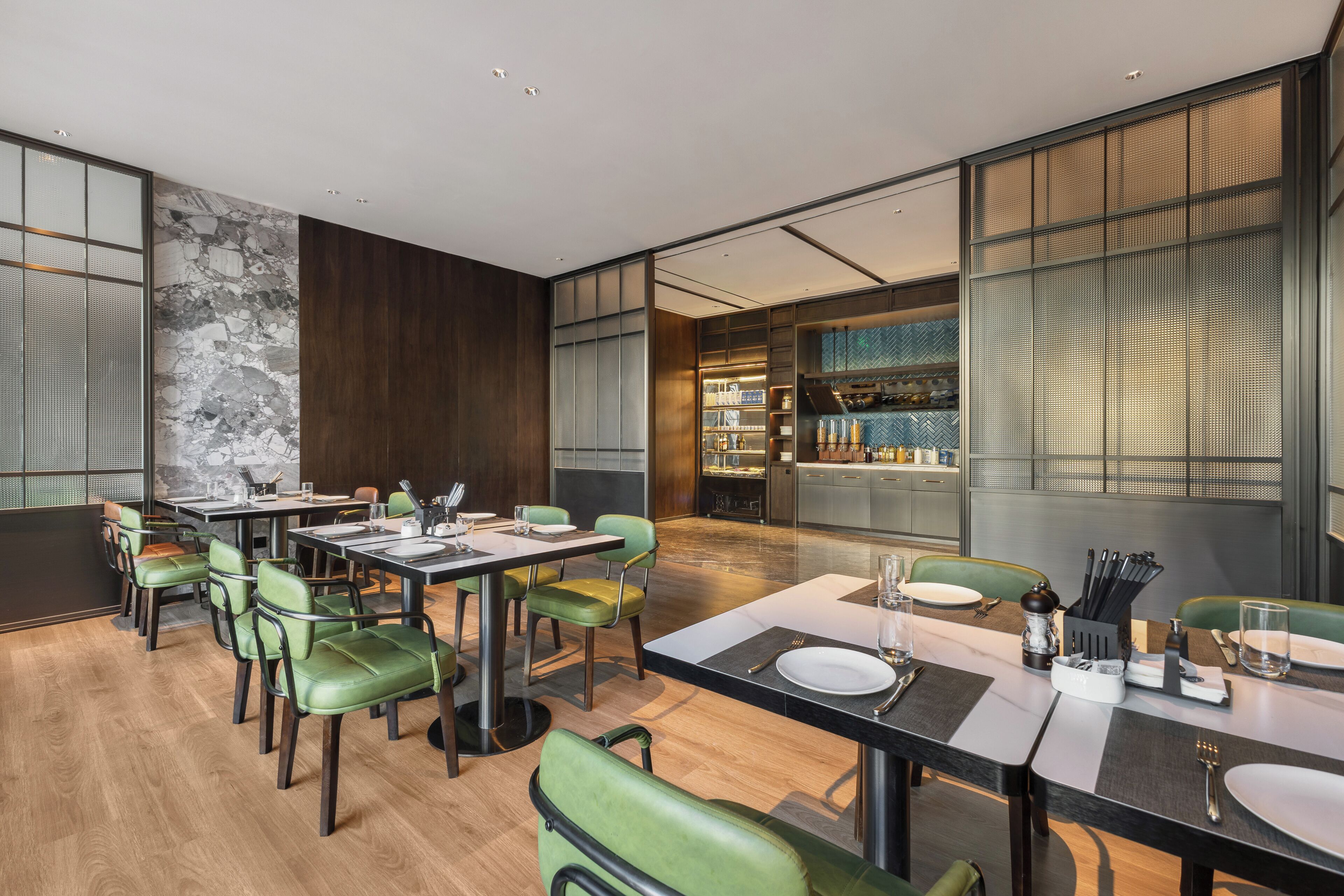 Un comedor moderno con una mesa larga, sillas verdes y una cocina al fondo.