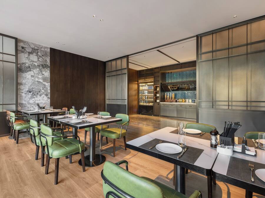 Un comedor moderno con una mesa larga, sillas verdes y una cocina al fondo.
