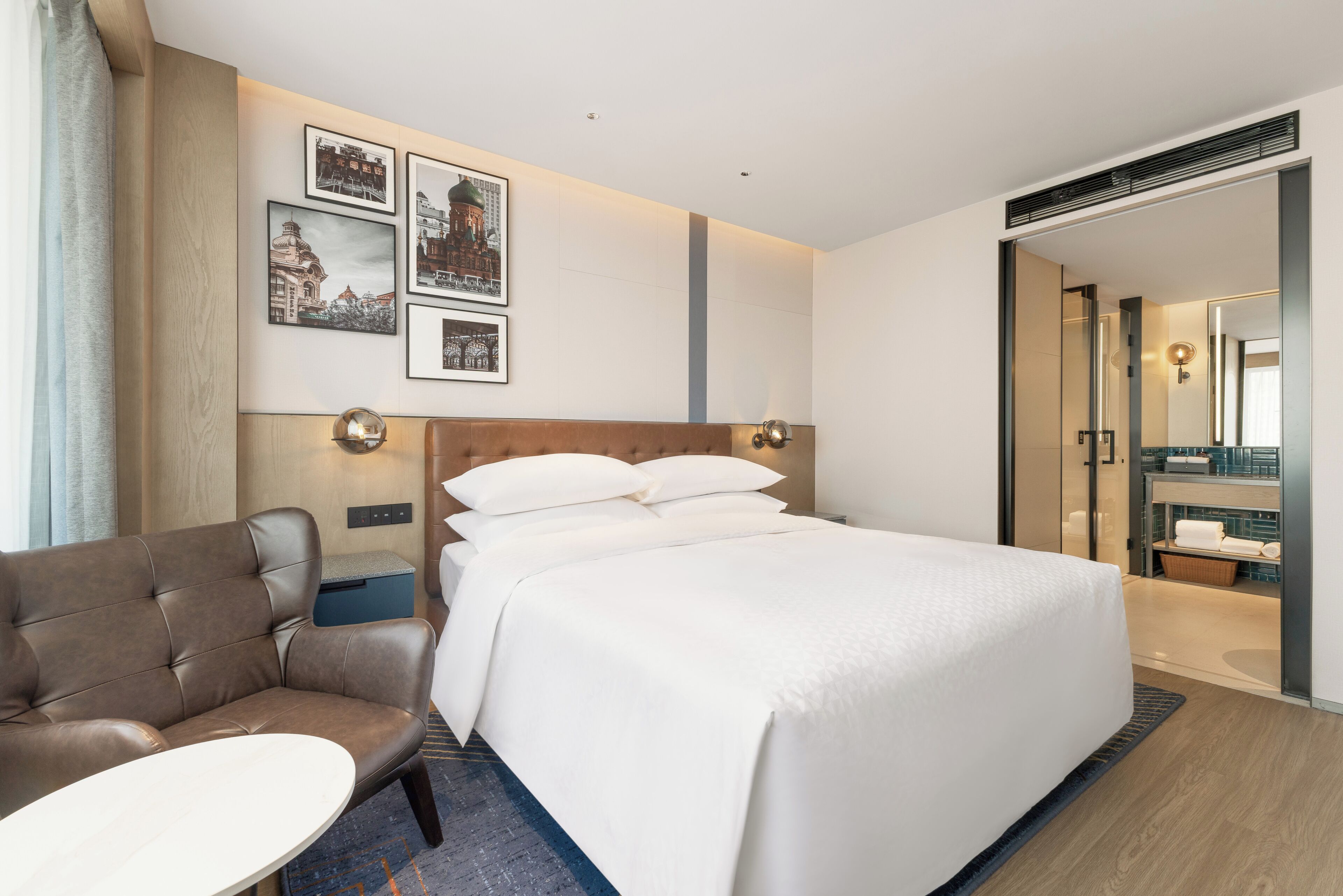 A hotel room with a bed, a sofa, a small table, and a wall-mounted TV.