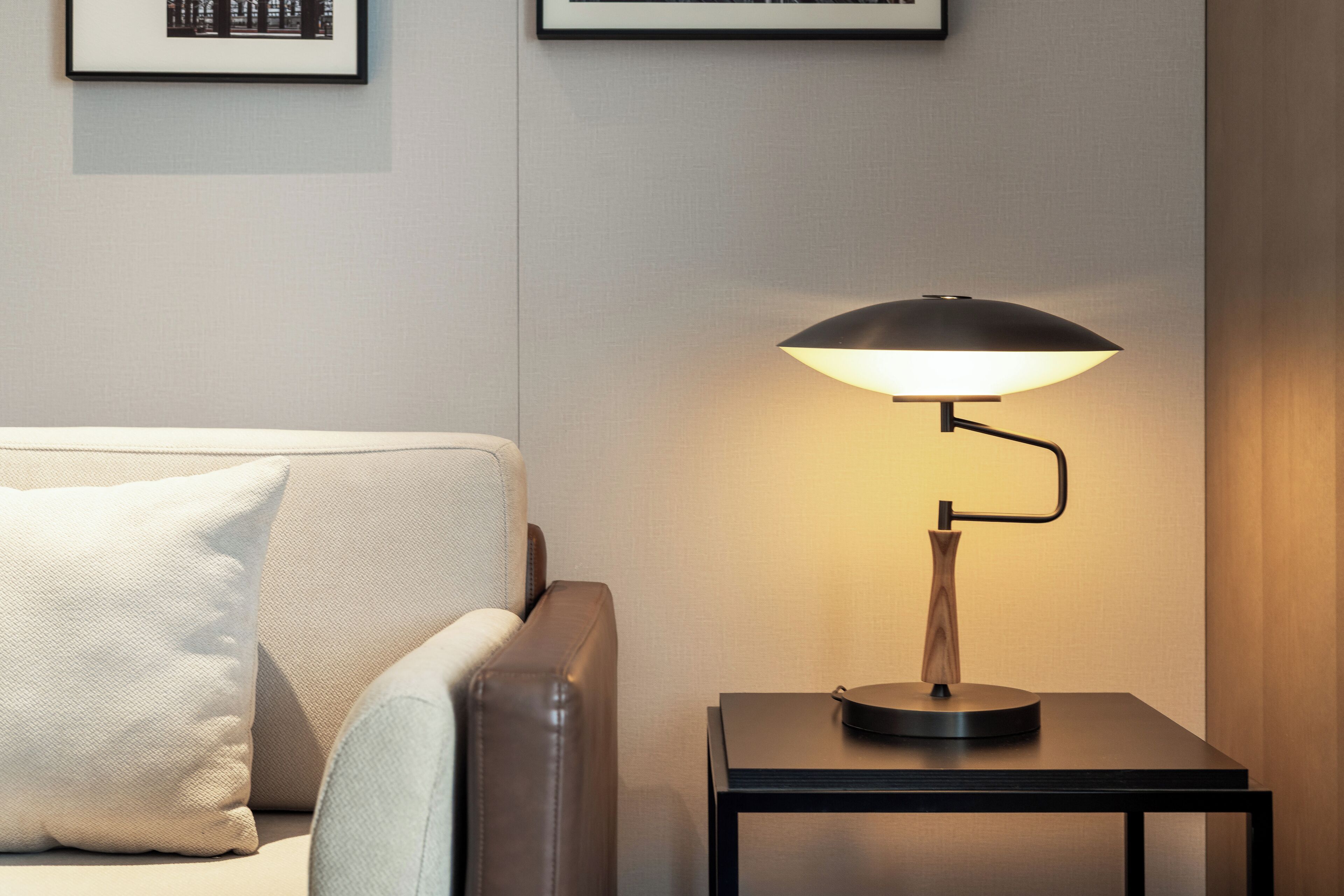 A modern room with a sofa, a side table with a lamp, and framed pictures on the wall.