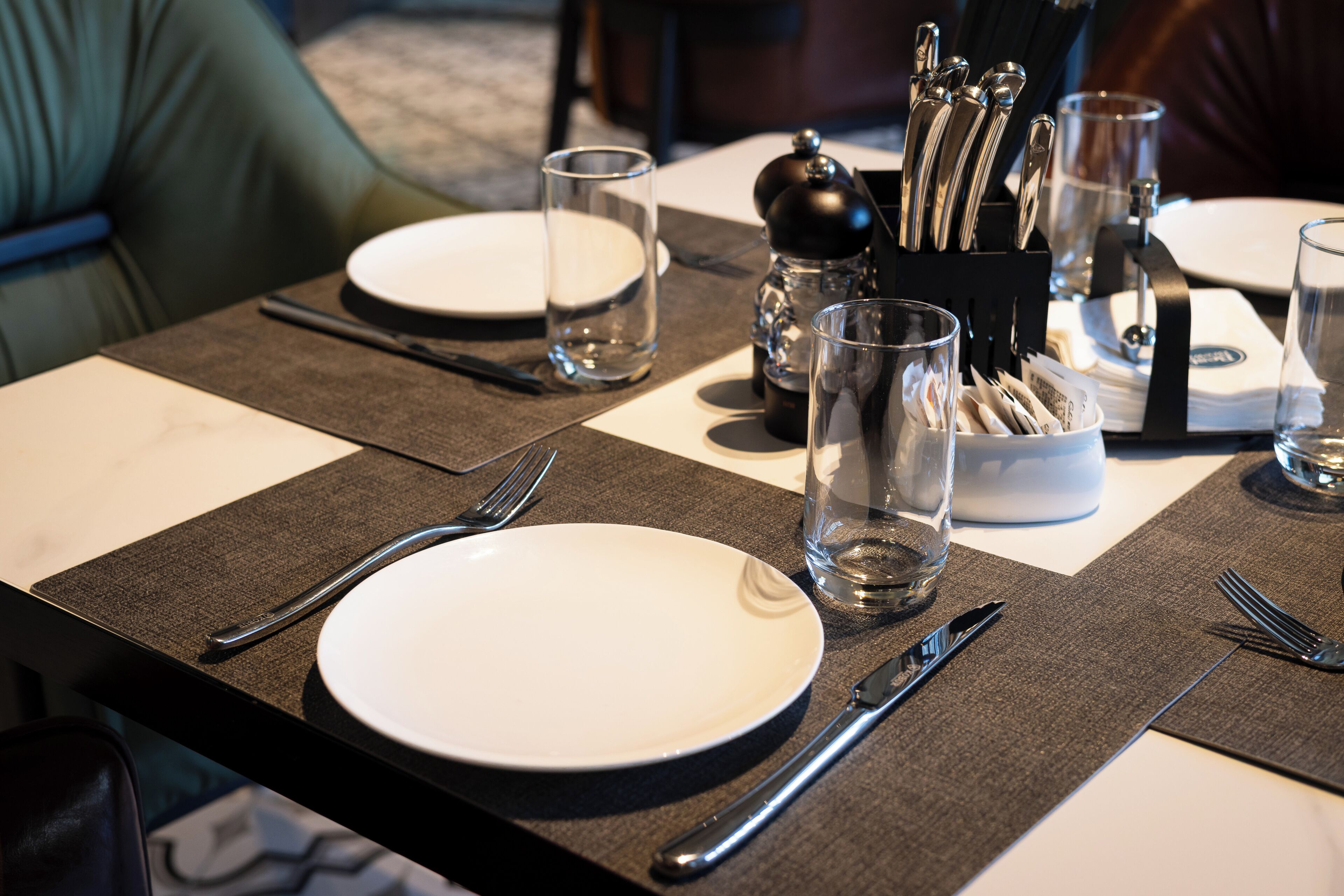 A neatly set dining table with plates, cutlery, glasses, and a salt and pepper set.
