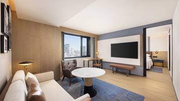 A modern hotel room with a sofa, a round table, a chair, a TV, and a city view.