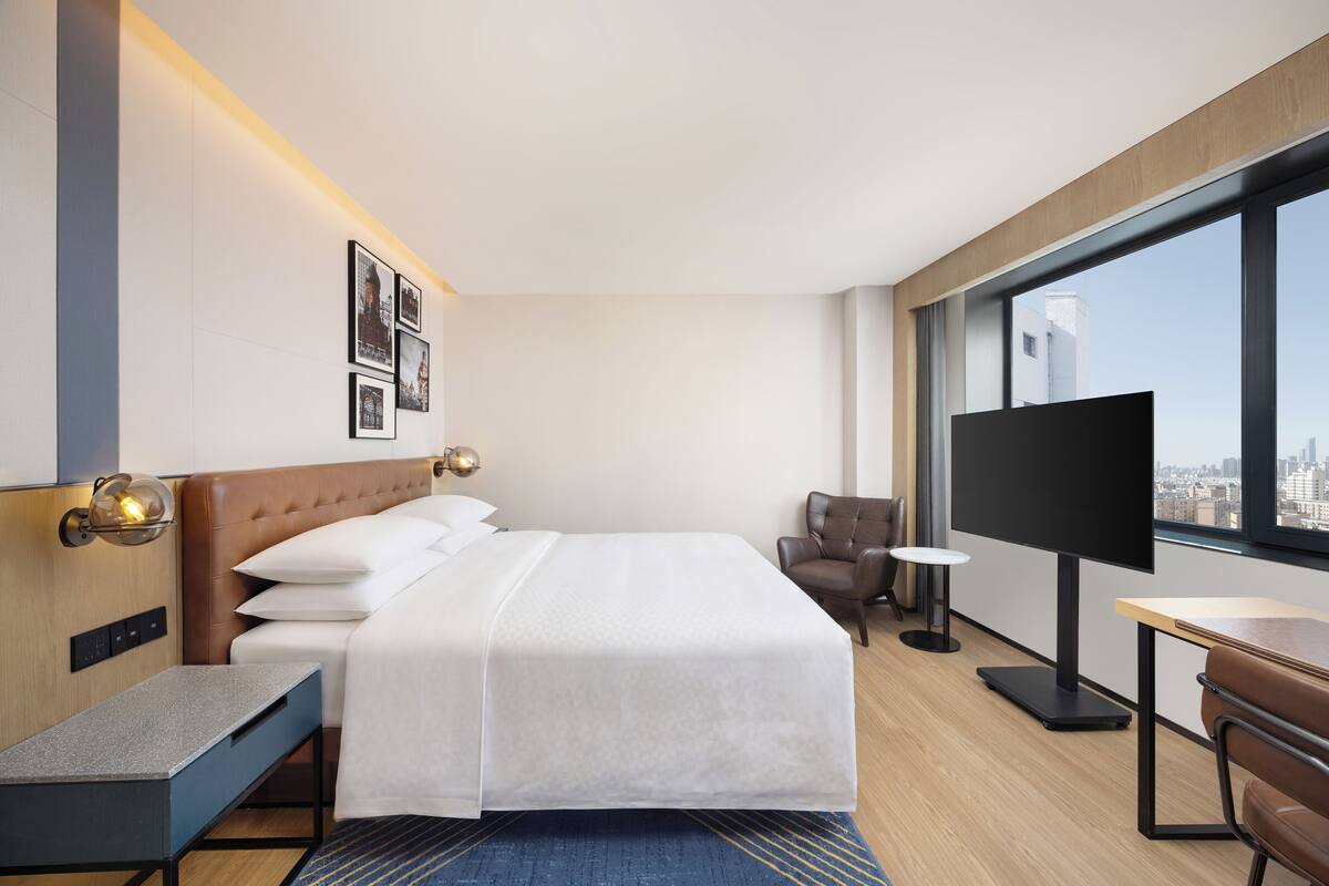 A hotel room with a bed, a desk, a chair, a TV, and a large window.
