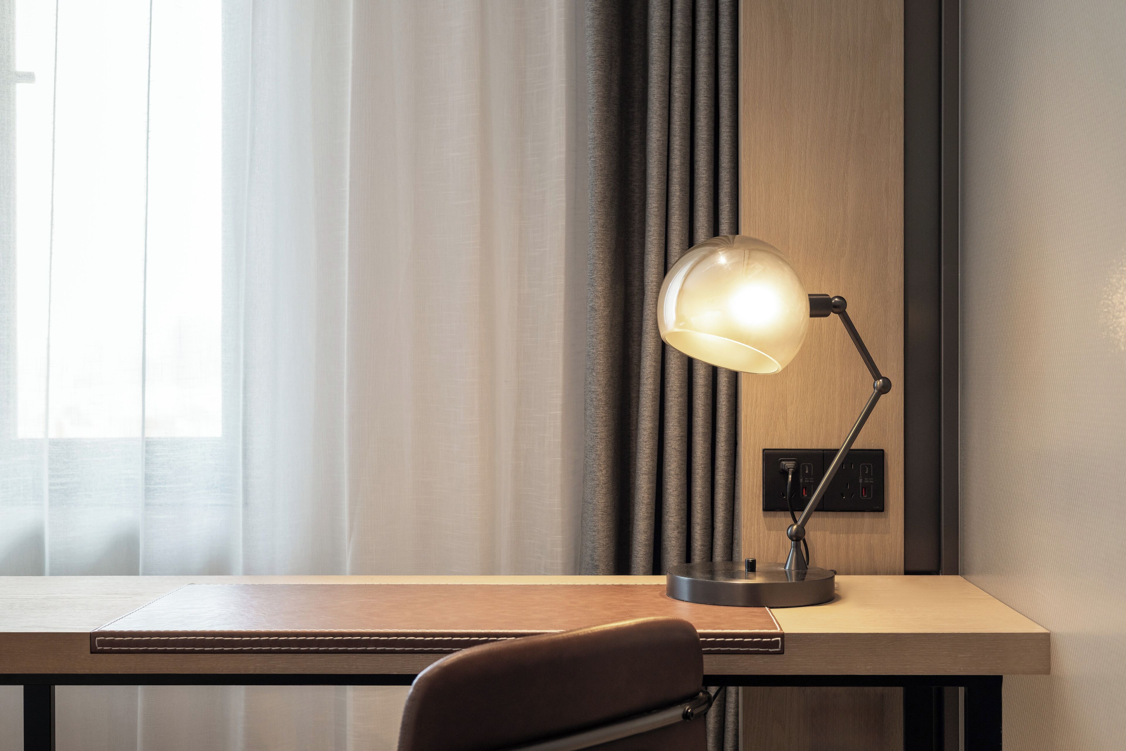 Un escritorio con una lámpara, una silla y una ventana con cortinas.