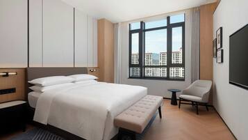 Ein modernes Hotelzimmer mit einem großen Bett, einem kleinen runden Tisch, einem Sessel und einem großen Fenster mit Blick auf die Stadt.