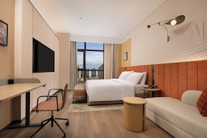 A hotel room with a bed, a desk, a chair, a small round table, and a sofa.