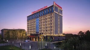 Un hôtel à plusieurs étages, reconnaissable à son grand panneau « Hilton Garden Inn », doté d’un parking et d’un espace paysager agrémenté d’arbres.