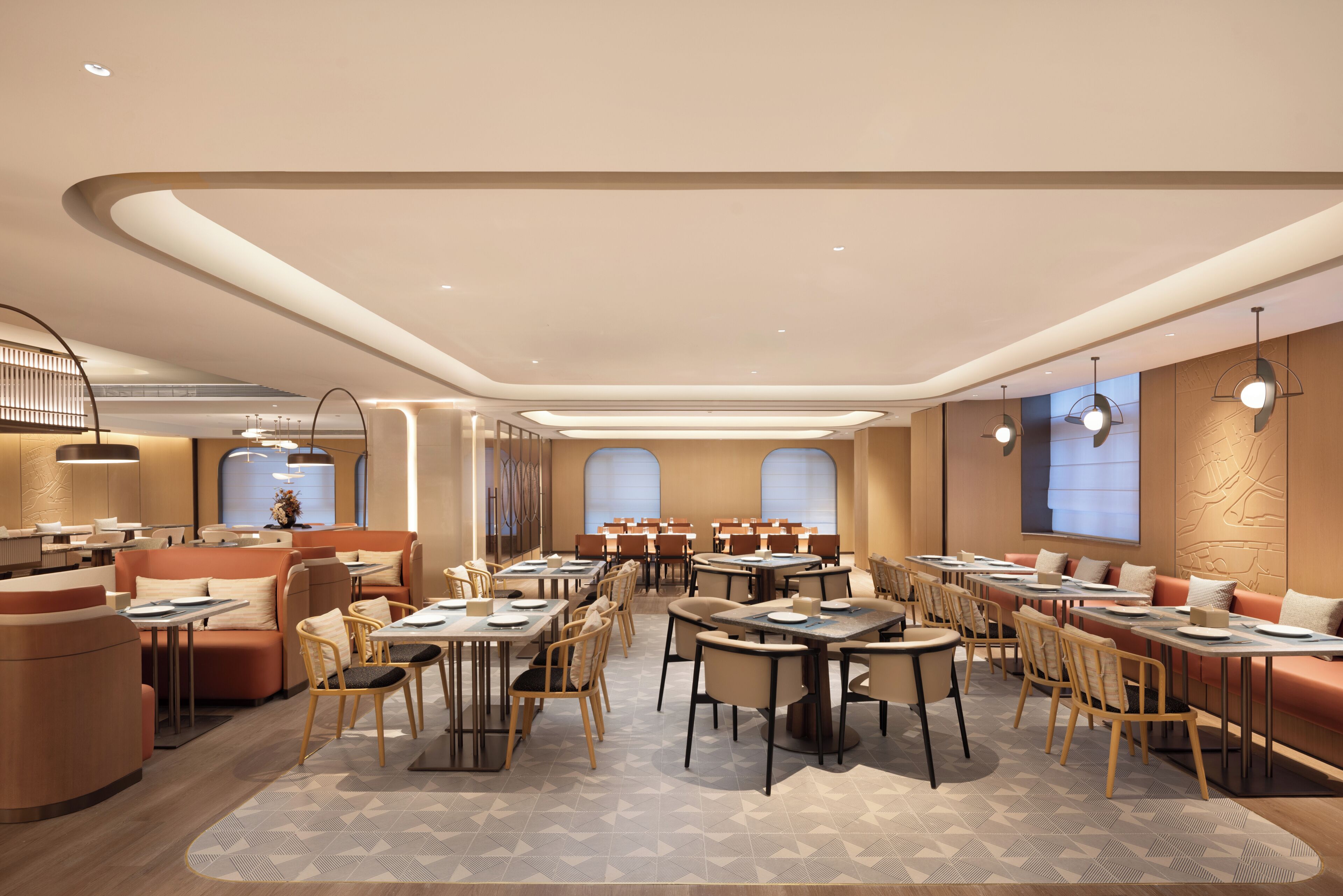 A modern hotel lobby with a central seating area, multiple tables, and a large screen.