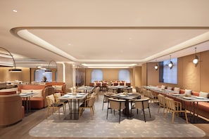 A modern hotel lobby with a central seating area, multiple tables, and a large screen.