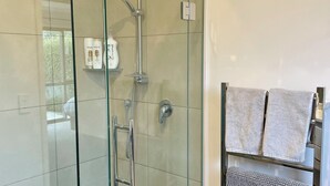 A modern bathroom with a glass-enclosed shower, a towel rack with two towels, and a shelf with toiletries. - Stunning views in quiet location, luggate. 10 mins out of Wanaka. (Luggate)