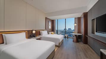 Ein Hotelzimmer mit zwei Betten, einem Esstisch, einem Fernseher und Blick auf die Stadt.