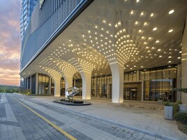 Un edificio moderno con un diseño de techo singular, amplias ventanas y una escultura central.
