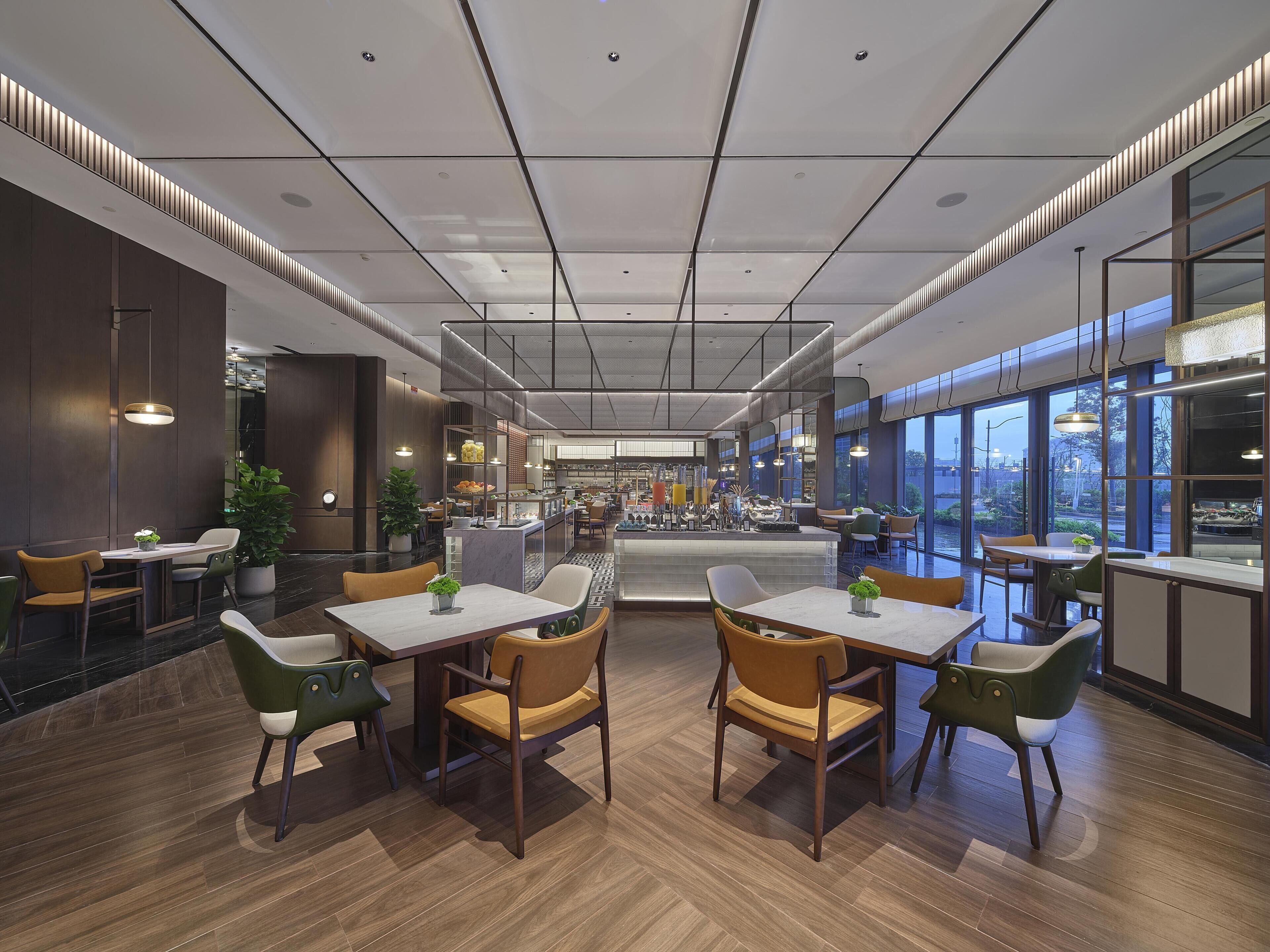 A modern restaurant with wooden flooring, multiple seating areas, and large windows offering views.