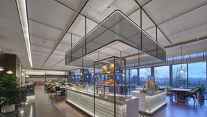 Un restaurant moderne doté d’un bar central, de grandes fenêtres et d’un plafond haut.