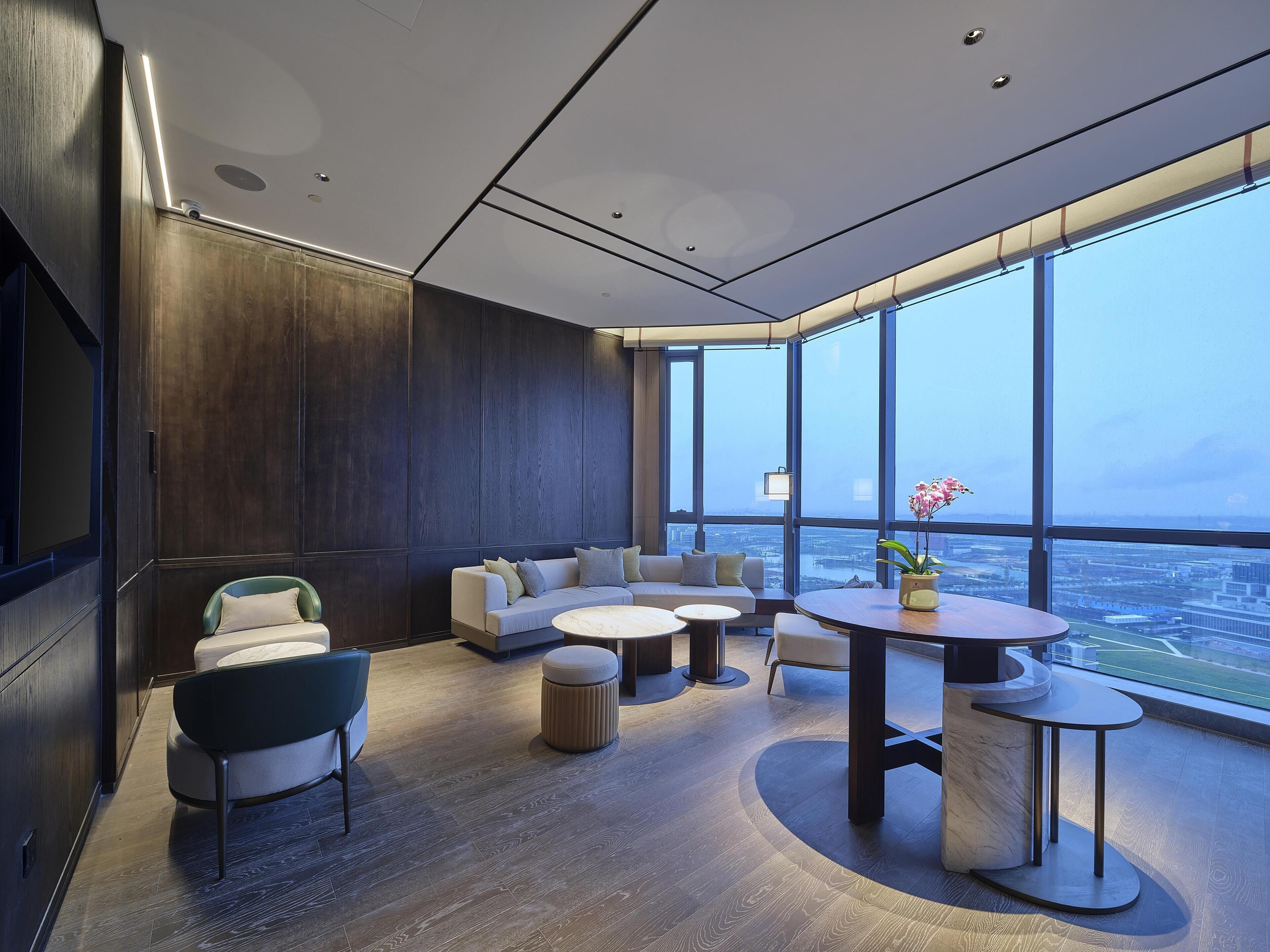 A modern lounge with a large window, a sofa set, a round table, and a small plant.