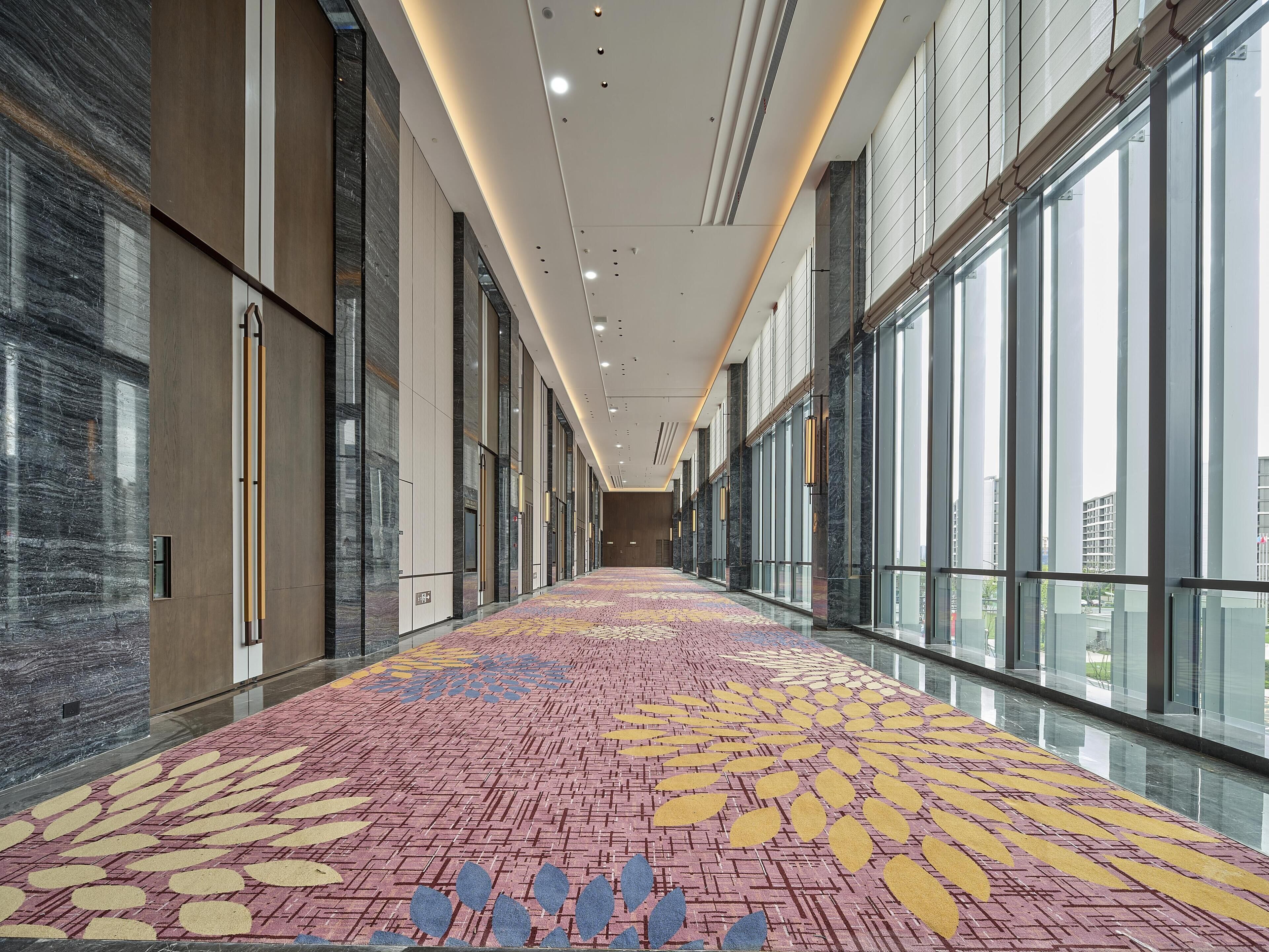 A long corridor with patterned carpet, large windows, and modern interior design.