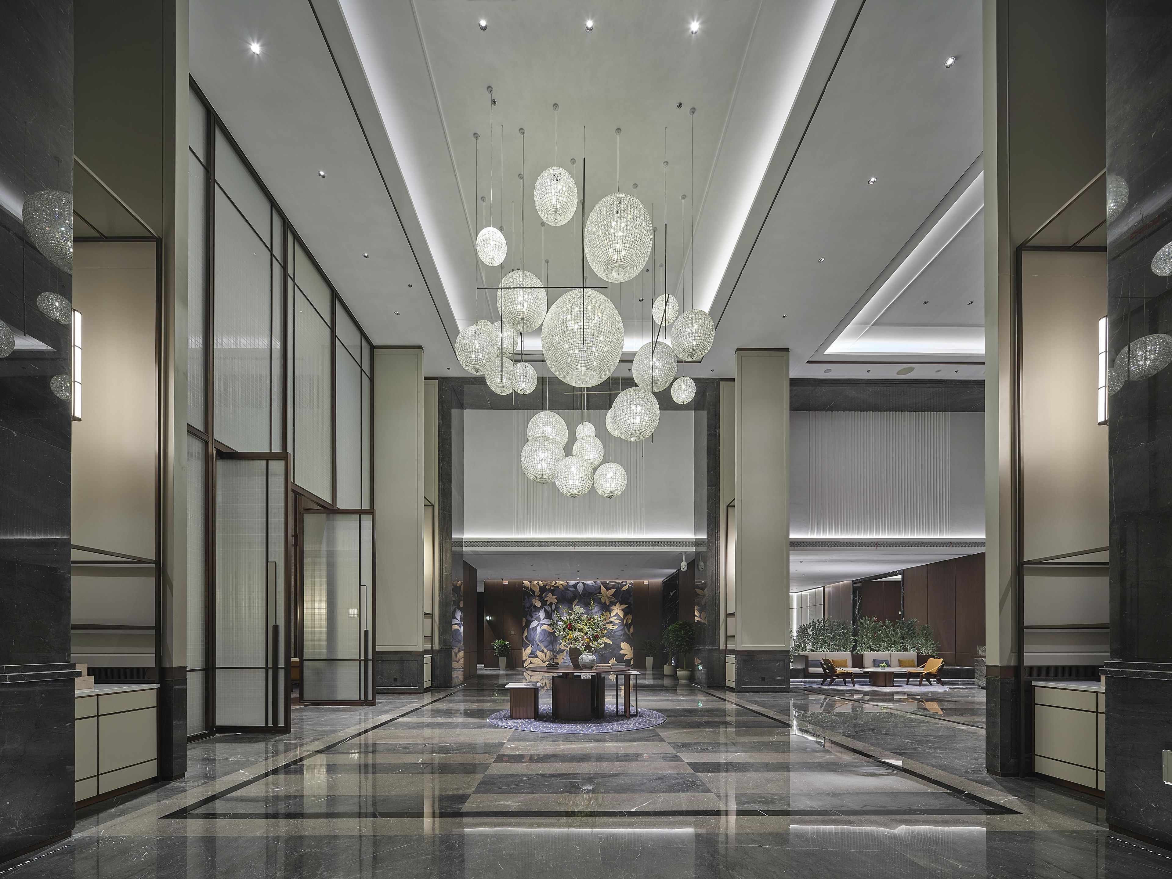 A modern lobby with a checkered floor, large windows, and a central seating area with plants.