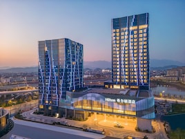 Un hotel moderno con una fachada curva y varios pisos, rodeado por un paisaje urbano y una masa de agua.