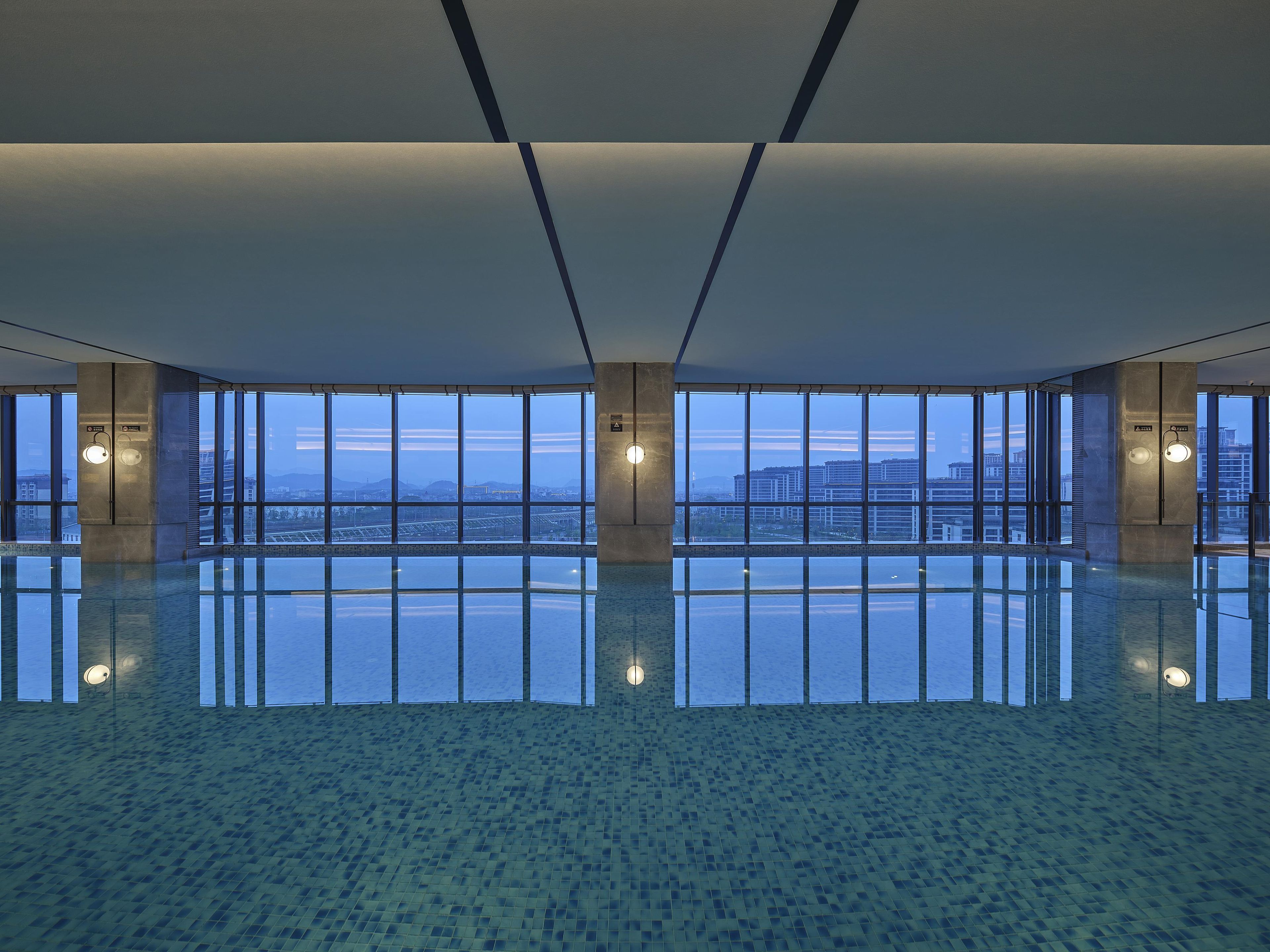 Un espacio interior amplio con un piso reflectante, ventanas grandes que ofrecen vistas panorámicas de la ciudad y un diseño arquitectónico moderno.