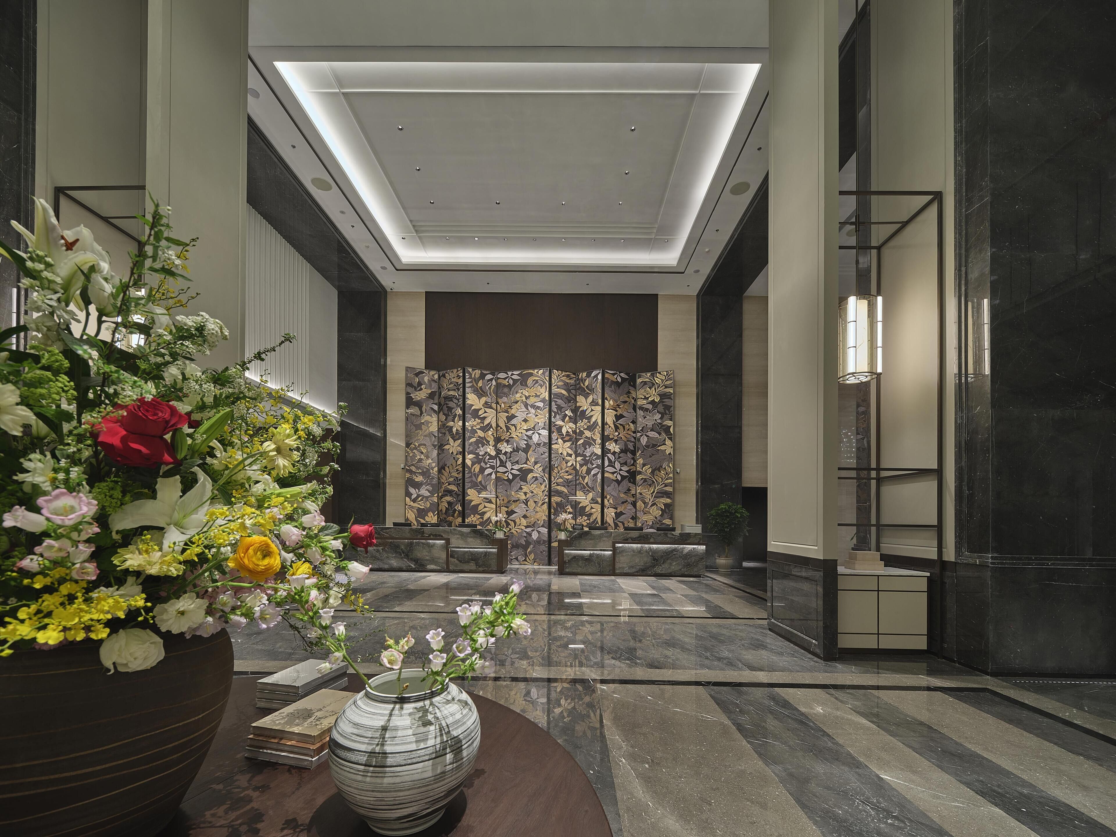 A modern lobby with a large floral arrangement, a decorative screen, and a reception desk.