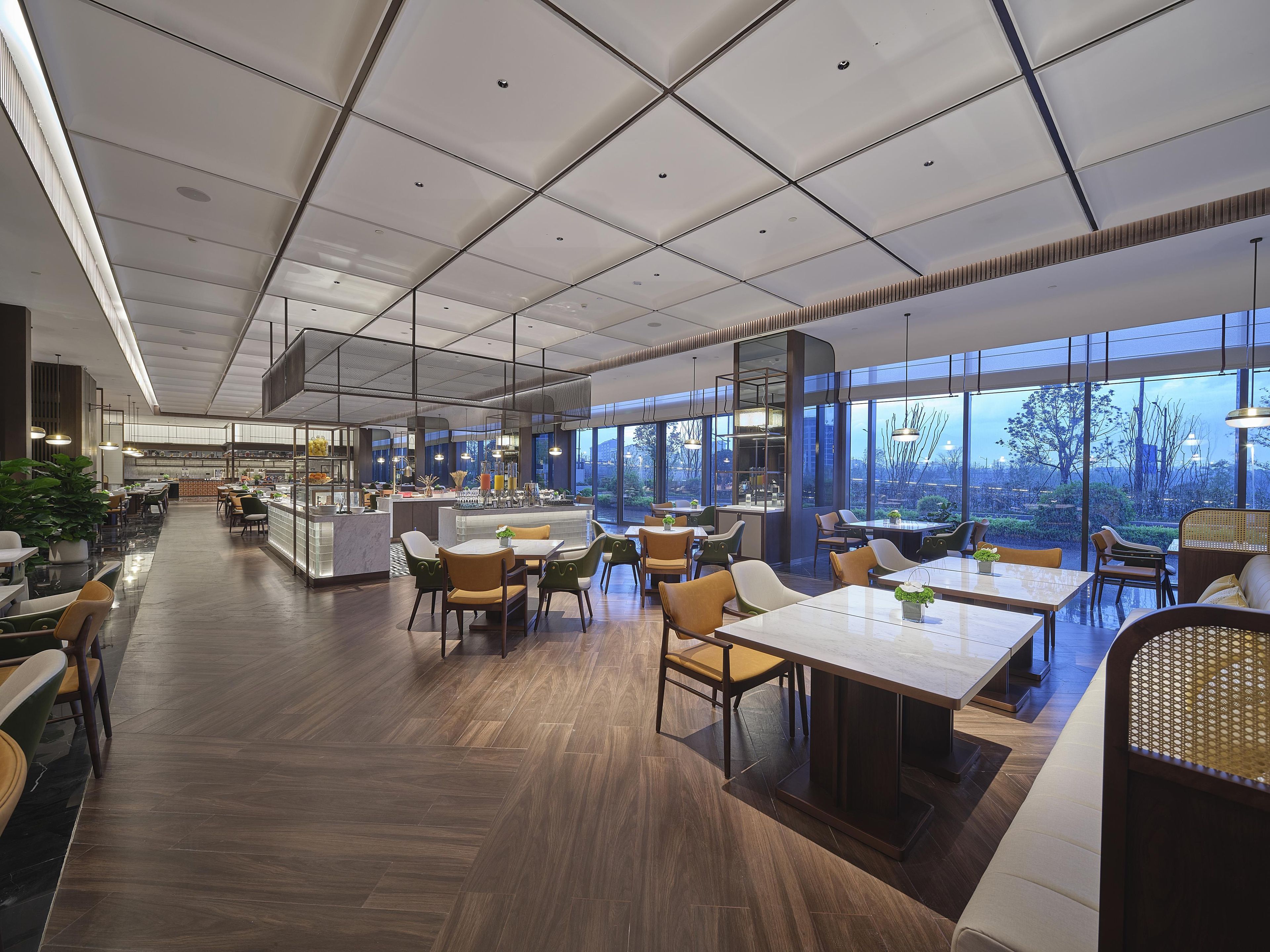 Ein geräumiges Restaurant mit hoher Decke, moderner Beleuchtung und großen Fenstern, die einen Blick ins Freie bieten.
