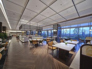 A spacious restaurant with a high ceiling, modern lighting, and large windows offering a view of the outdoors. - Hilton Quzhou (Quzhou)