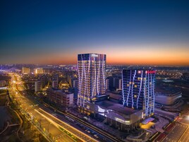 Un hotel moderno de gran altura con varios pisos, rodeado por un paisaje urbano al anochecer.