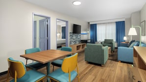 A hotel room with a dining table, chairs, a sofa, a TV, and a lamp. - Garner Hotel Madison Huntsville Airport by IHG (Madison)