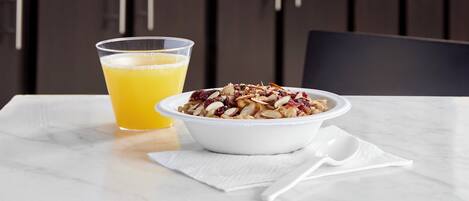 A breakfast setting with a bowl of cereal and a glass of orange juice on a marble table.