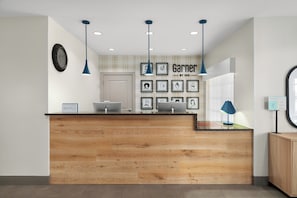 Un mostrador de recepción con acabado de madera, obras de arte enmarcadas en la pared y una lámpara colgante azul.