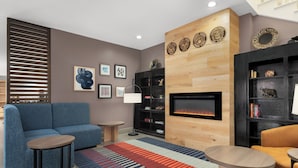 A modern living room with a sectional sofa, a fireplace, a bookshelf, and a patterned rug. - Garner Hotel Madison Huntsville Airport by IHG (Madison)